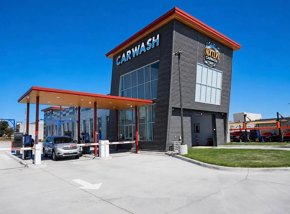 Gray car wash building with red trim, 'CARWASH' sign, and a silver SUV entering under a blue sky.