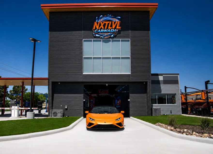 The NXTLVL Car Wash building in Grand Prairie, with an orange sports car pulling out of the wash tunnel